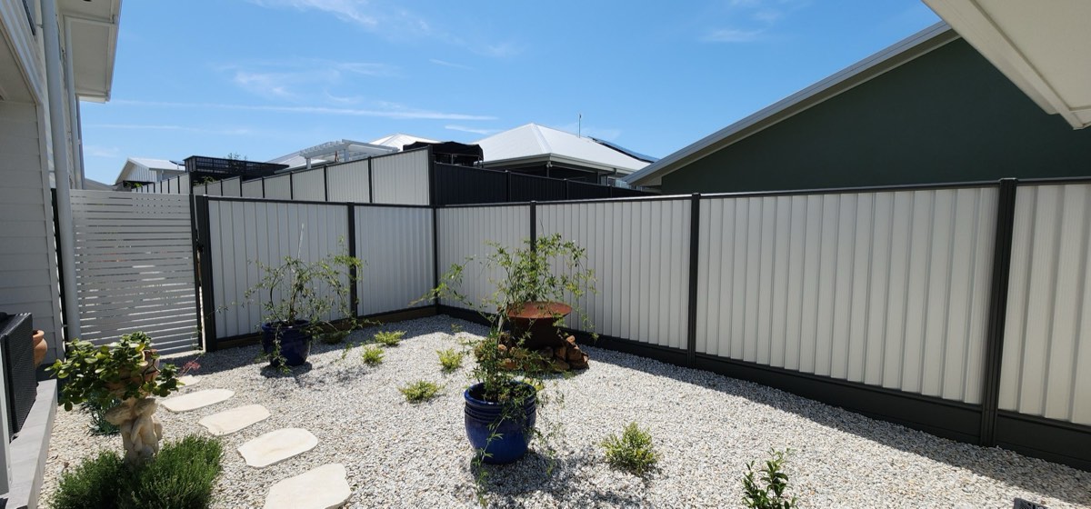 White Colorbond fence with dark posts around a landscaped backyard